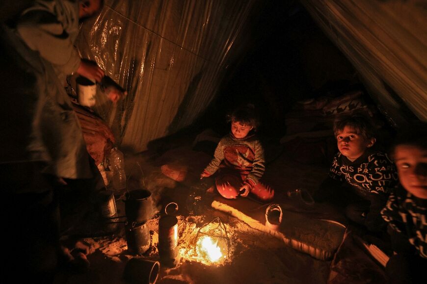 Displaced Palestinian children sit by the fire at a makeshift camp west of Rafah