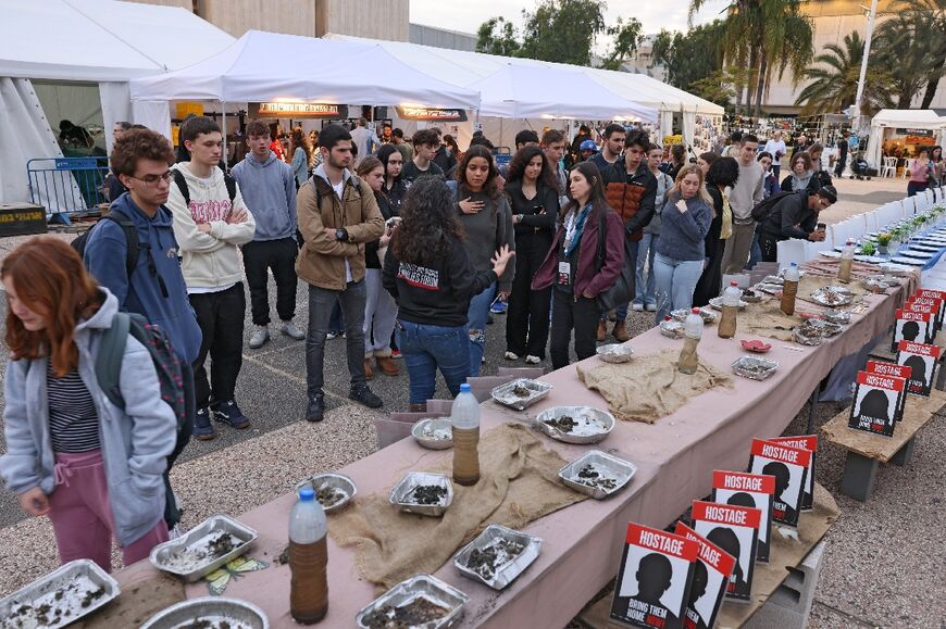 Visitors by a table covered in dirty water bottles and aluminium mess tins, to symbolise the hostages' captivity